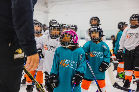 Young girl in ice hockey gear looking up at coach giving instruction. 