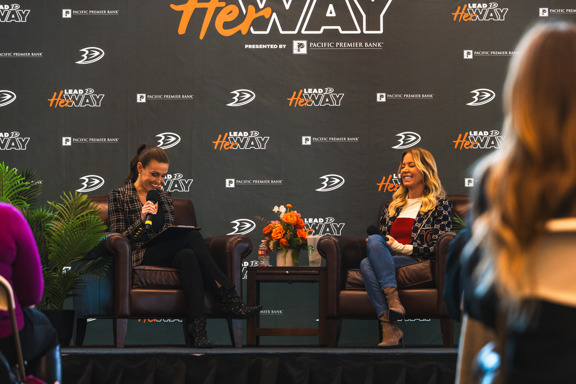 Jeannie Buss and Ally Lozof laughing on stage during a fireside chat.